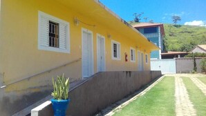 A yellow building with white shutters, a potted plant, and a paved pathway. - Pousada Dedo de Deus (Paraisopolis)