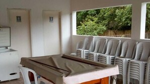 A pool table in a room with tiled flooring, white chairs, and a view of greenery outside. - Pousada Dedo de Deus (Paraisopolis)