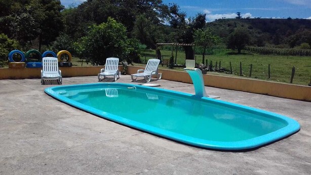 A rectangular swimming pool with a blue edge, surrounded by white lounge chairs. - Pousada Dedo de Deus (Paraisopolis)