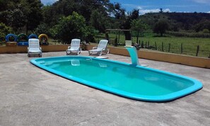 Una piscina rectangular con borde azul, rodeada de sillas reclinables blancas.