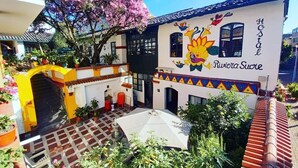 A hotel with a colorful mural, a courtyard with potted plants, and a traditional tiled roof. - Hostal Riviera Sucre (Otavalo)