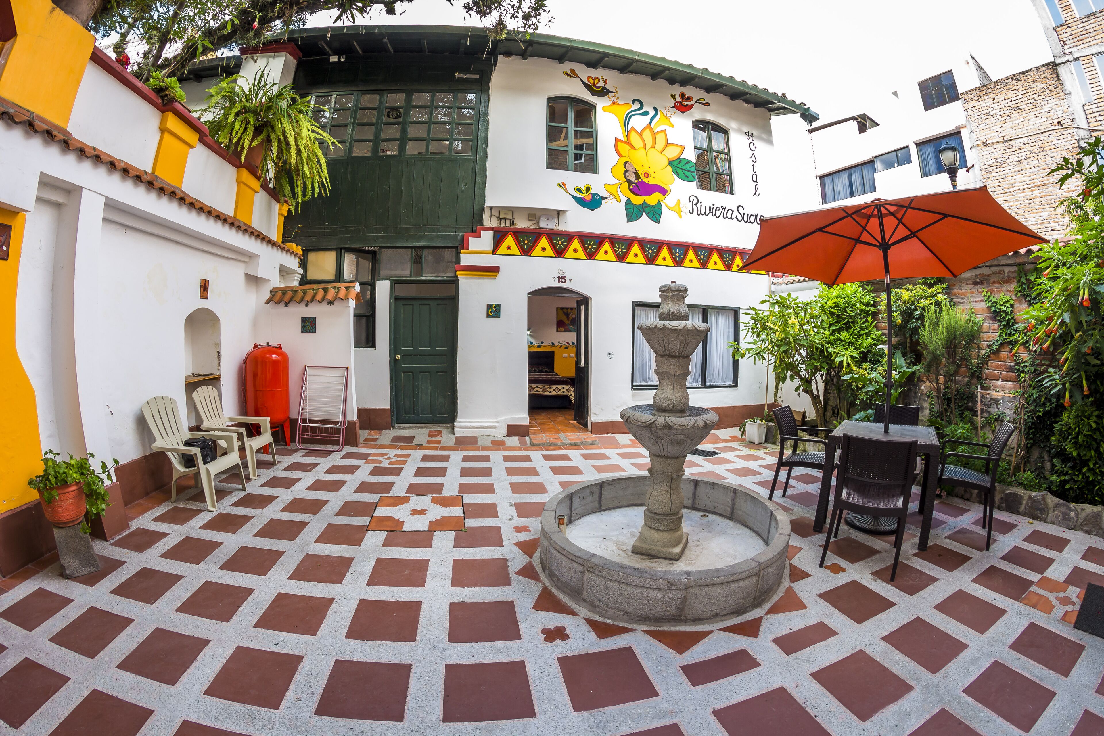 A courtyard with a fountain, outdoor seating, and a building with a mural.