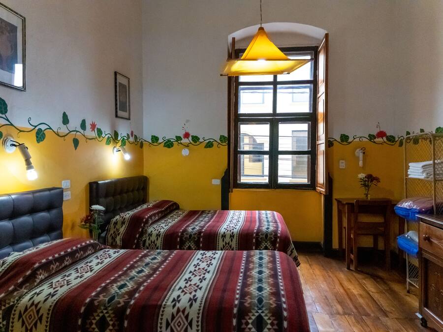 Una habitación con dos camas, suelo de madera, ventana con vistas y una lámpara colgante.