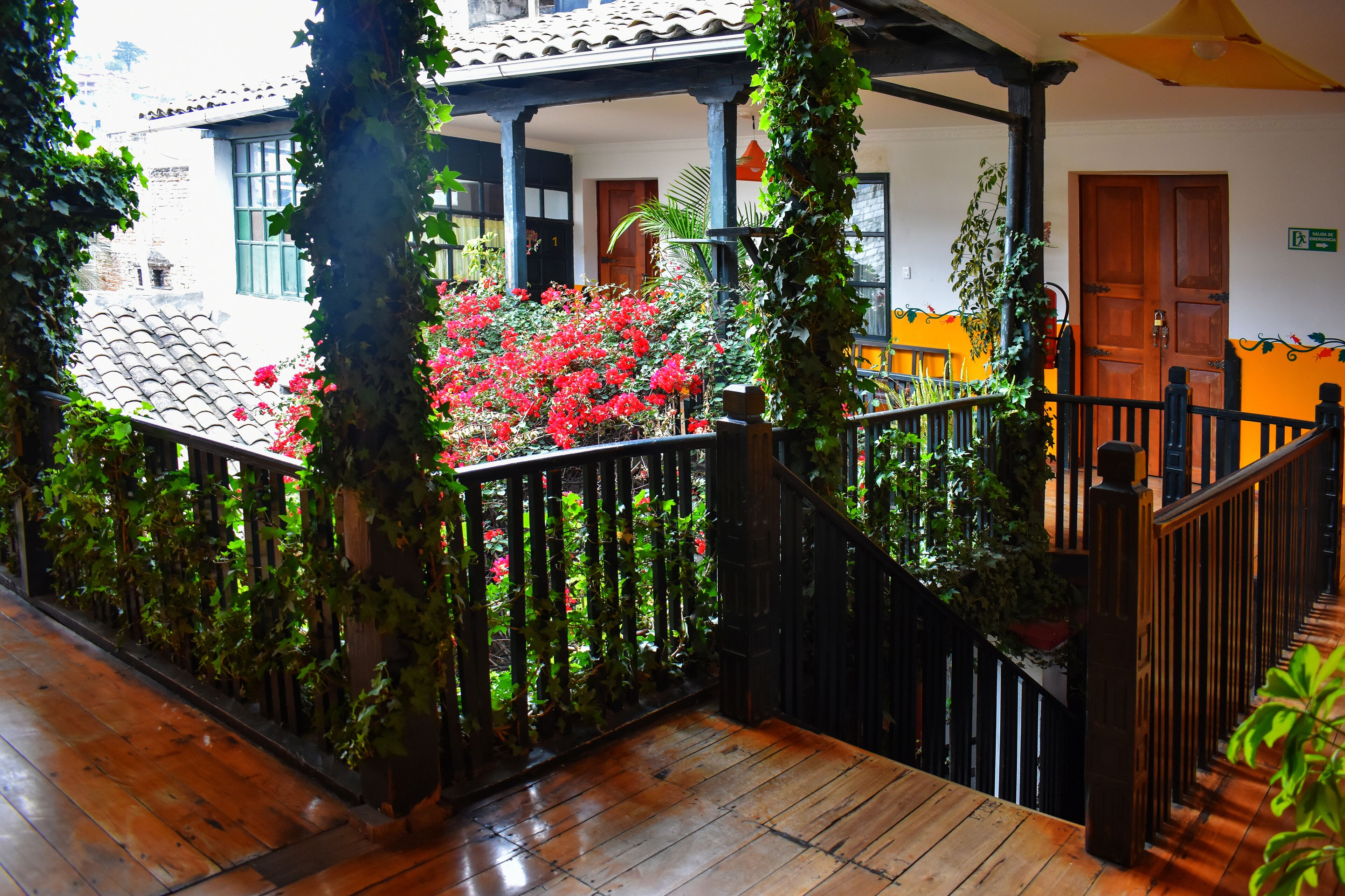 A wooden staircase with a metal railing, surrounded by greenery and red flowers.