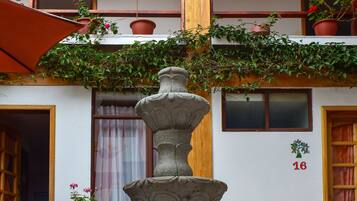 A courtyard with a stone fountain, two chairs, and a wooden door.