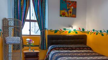 A room with a bed, a window with colorful curtains, a hanging light fixture, and a wall decoration.