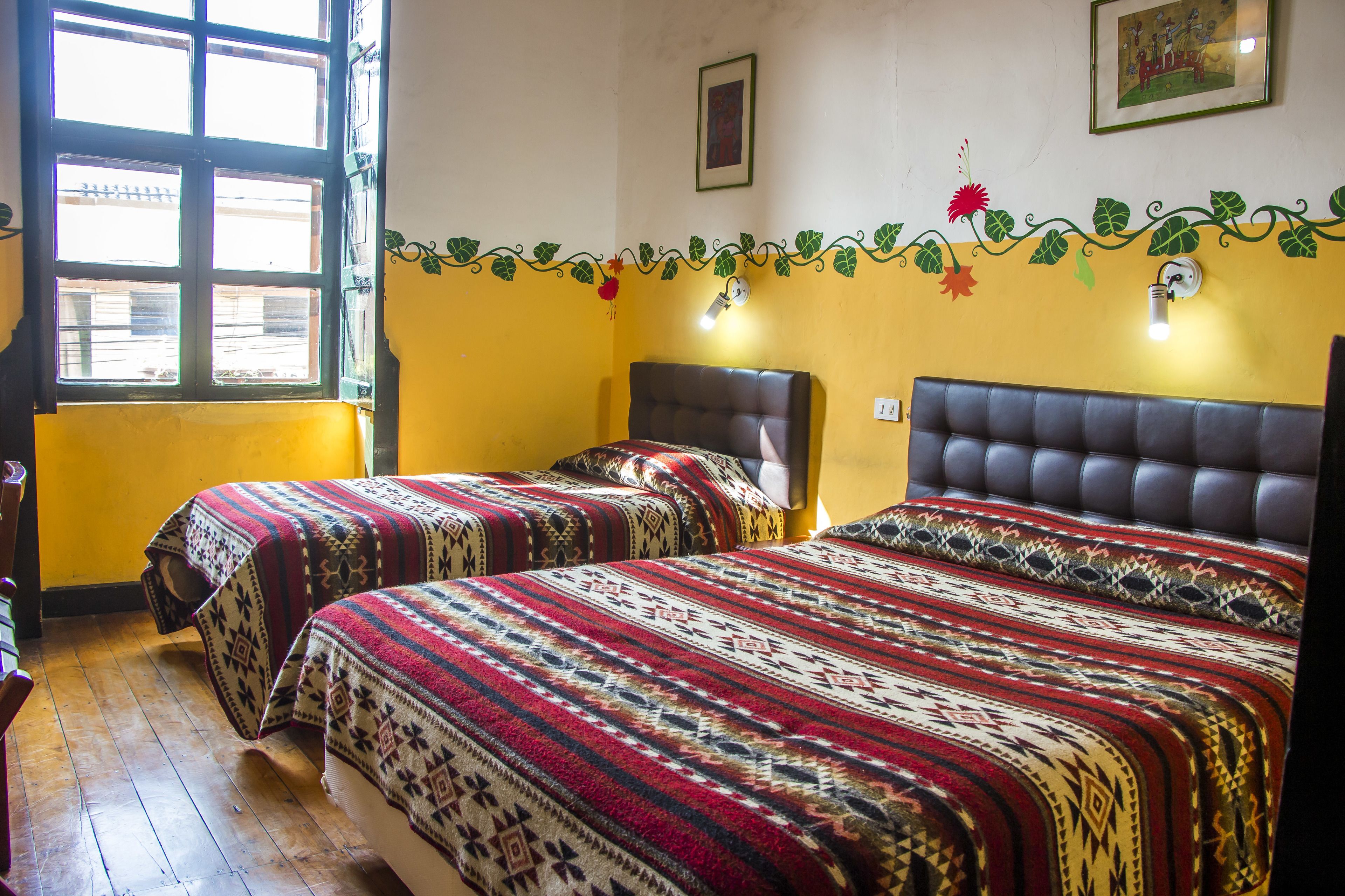 A room with two beds, a window, and a wall with a decorative vine.