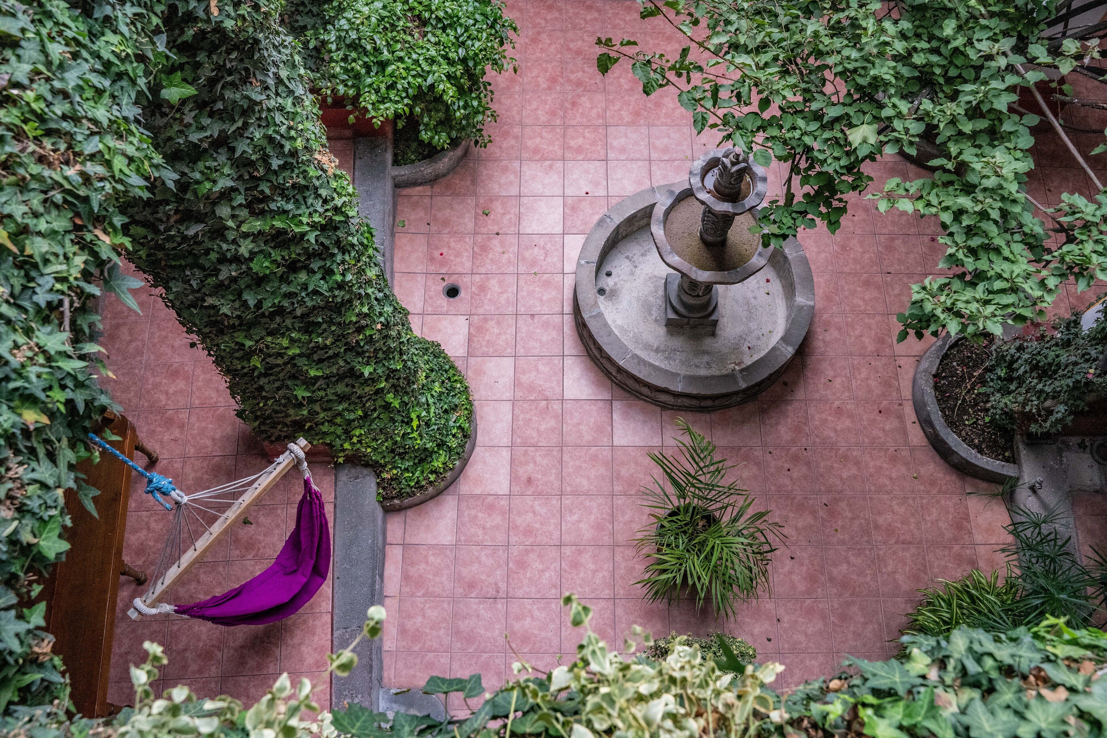 A courtyard with a hammock, a fountain, and various potted plants.