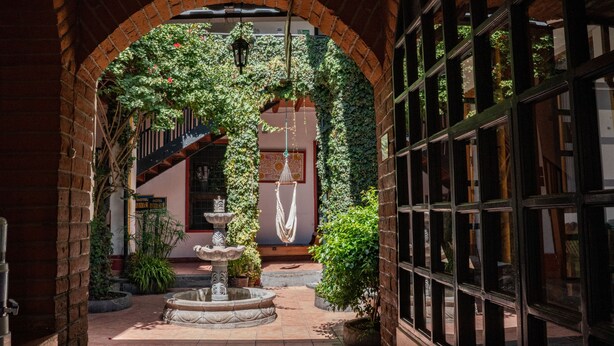 An arched brick corridor with a fountain, potted plants, and a hanging hammock. - Hostal Riviera Sucre (Otavalo)