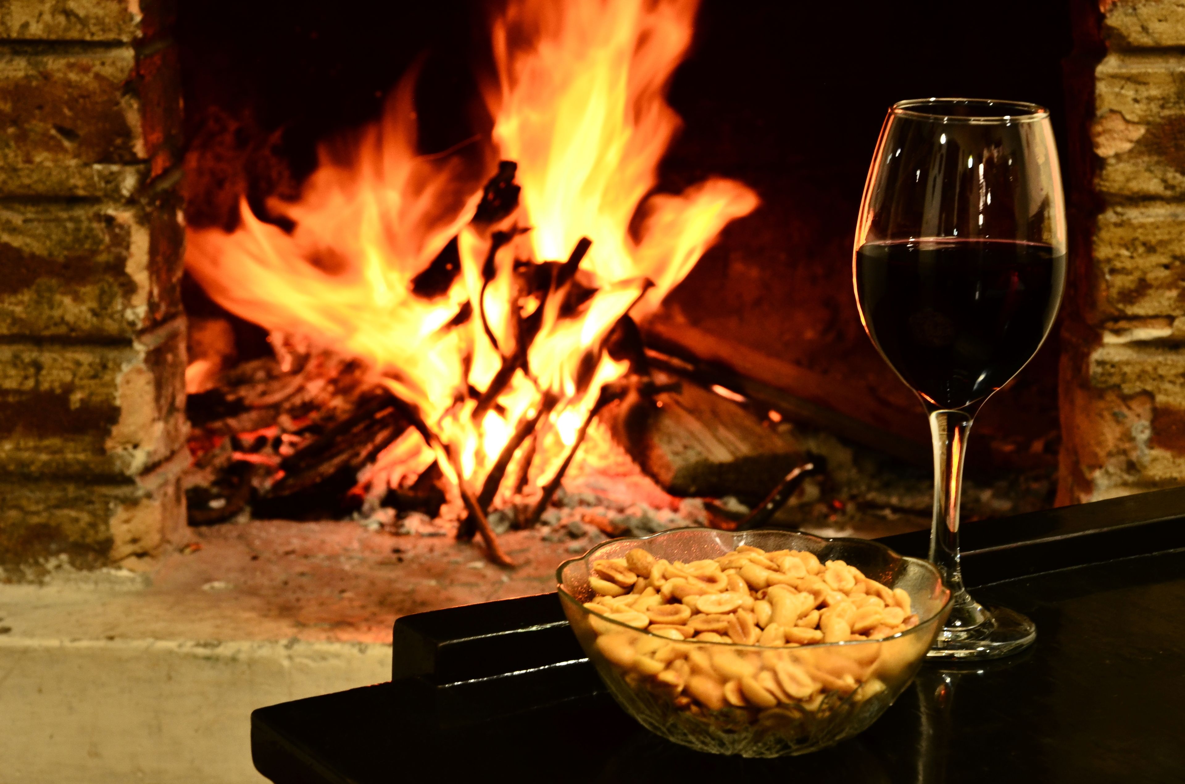 Ein Glas Rotwein und eine Schale Snacks vor einem Kamin mit Feuer.