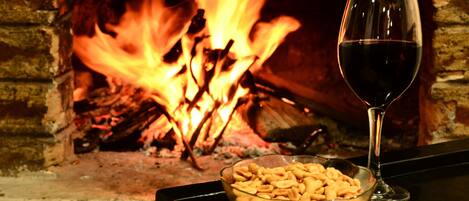 Ein Glas Rotwein und eine Schale Snacks vor einem Kamin mit Feuer.