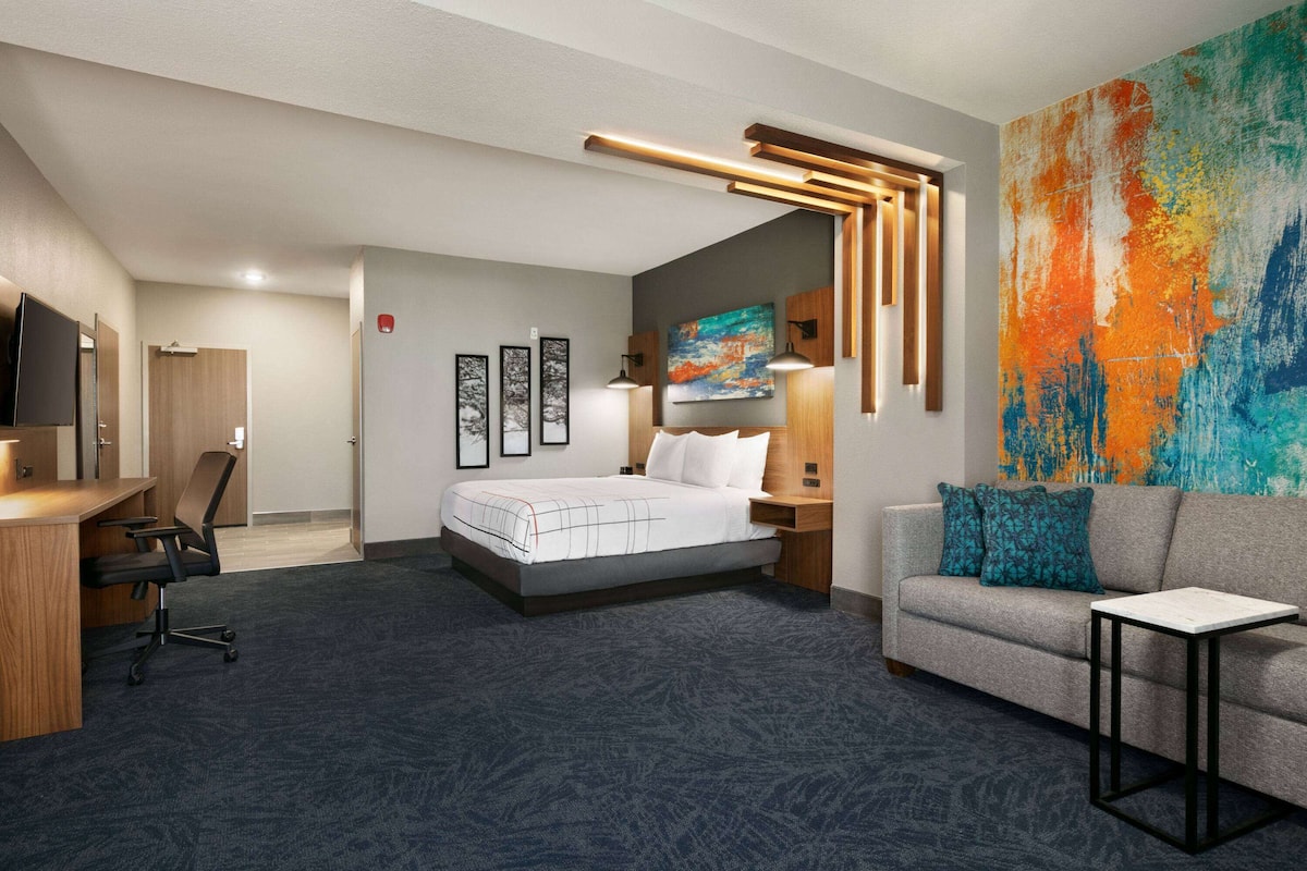 Una habitación de hotel con una cama, un escritorio, un sofá y un cuadro abstracto grande.