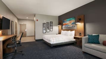 A hotel room with a bed, a desk, a chair, a sofa, a TV, and artwork on the walls.
