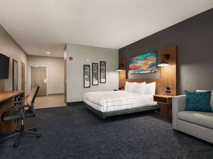 A hotel room with a bed, a desk, a chair, a sofa, a TV, and artwork on the walls.