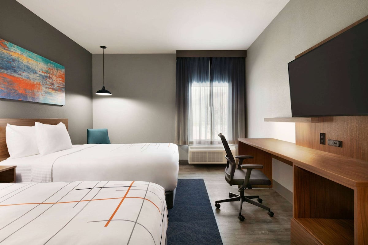 Habitación de hotel con dos camas, un escritorio, una silla, un televisor y un amplio ventanal con cortinas.