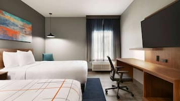 A hotel room with two beds, a desk, a chair, a TV, and a large window with curtains.