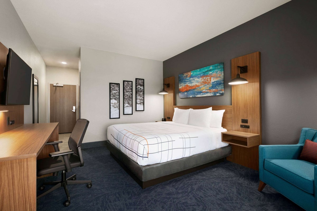 Habitación de hotel con cama, escritorio, silla, televisor y obras de arte en las paredes.