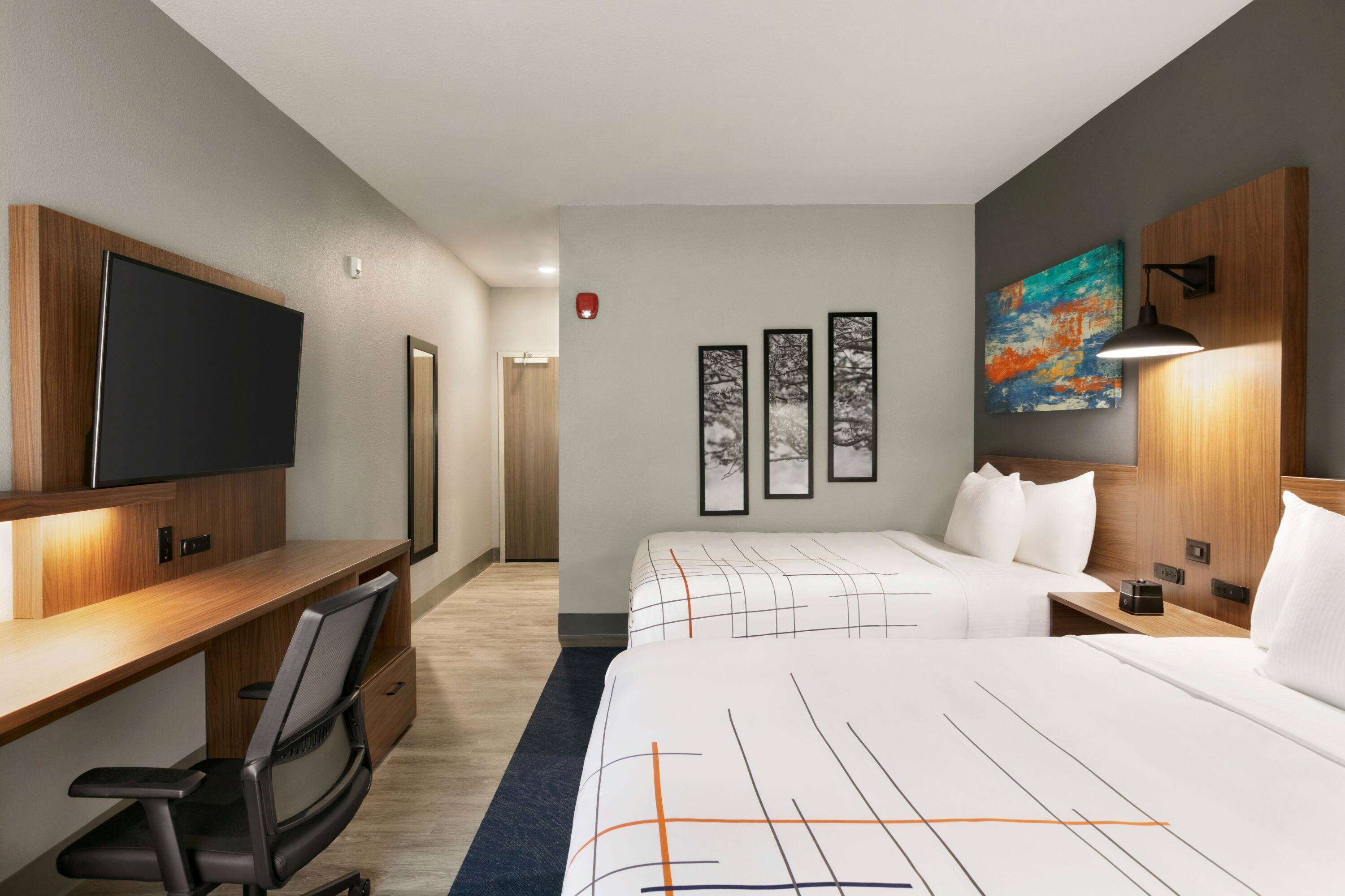 Habitación de hotel con cama, escritorio, silla, televisor, obras de arte y mesita de noche.