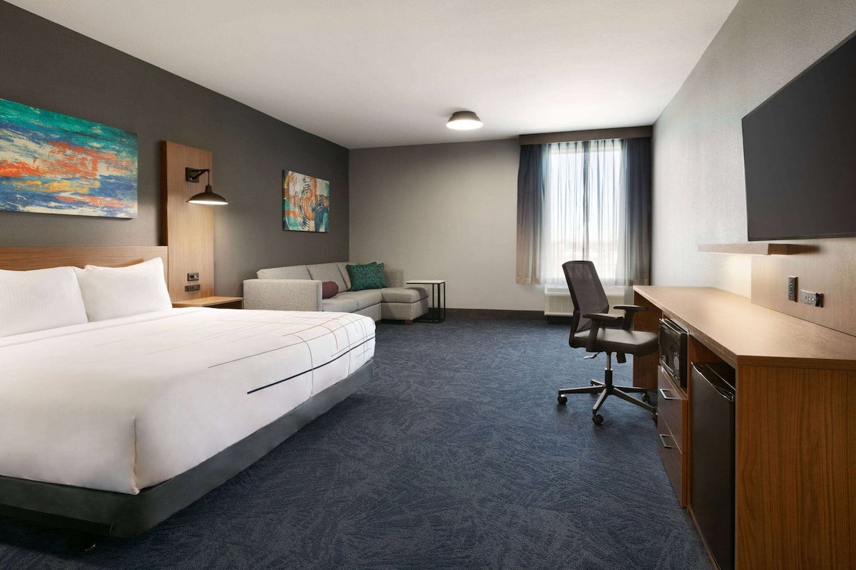 Habitación de hotel con una cama grande, un escritorio, una silla, una mesita y un sofá.