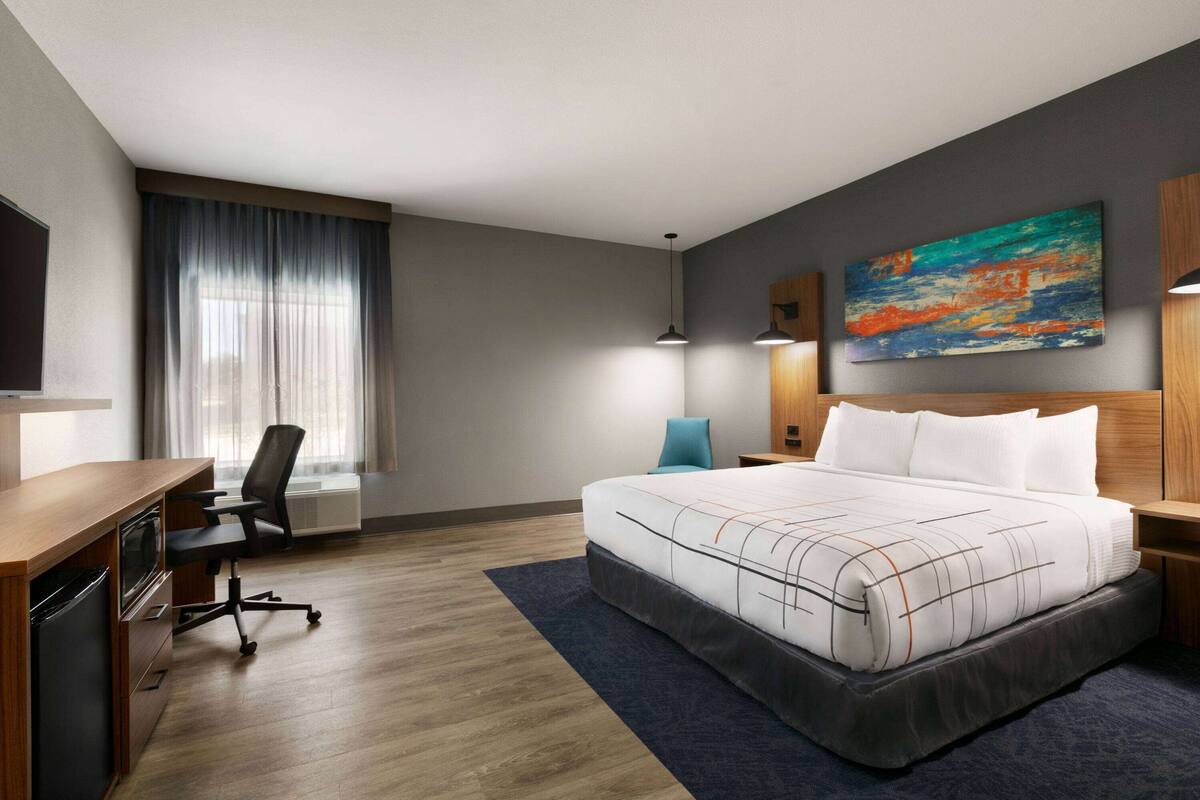 Habitación de hotel con cama, escritorio, silla y una obra de arte en la pared.