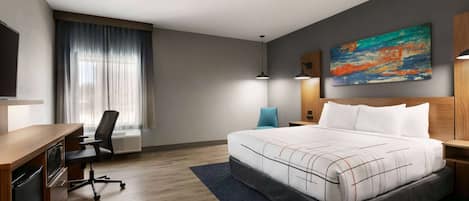 A hotel room with a bed, desk, chair, and artwork on the wall.