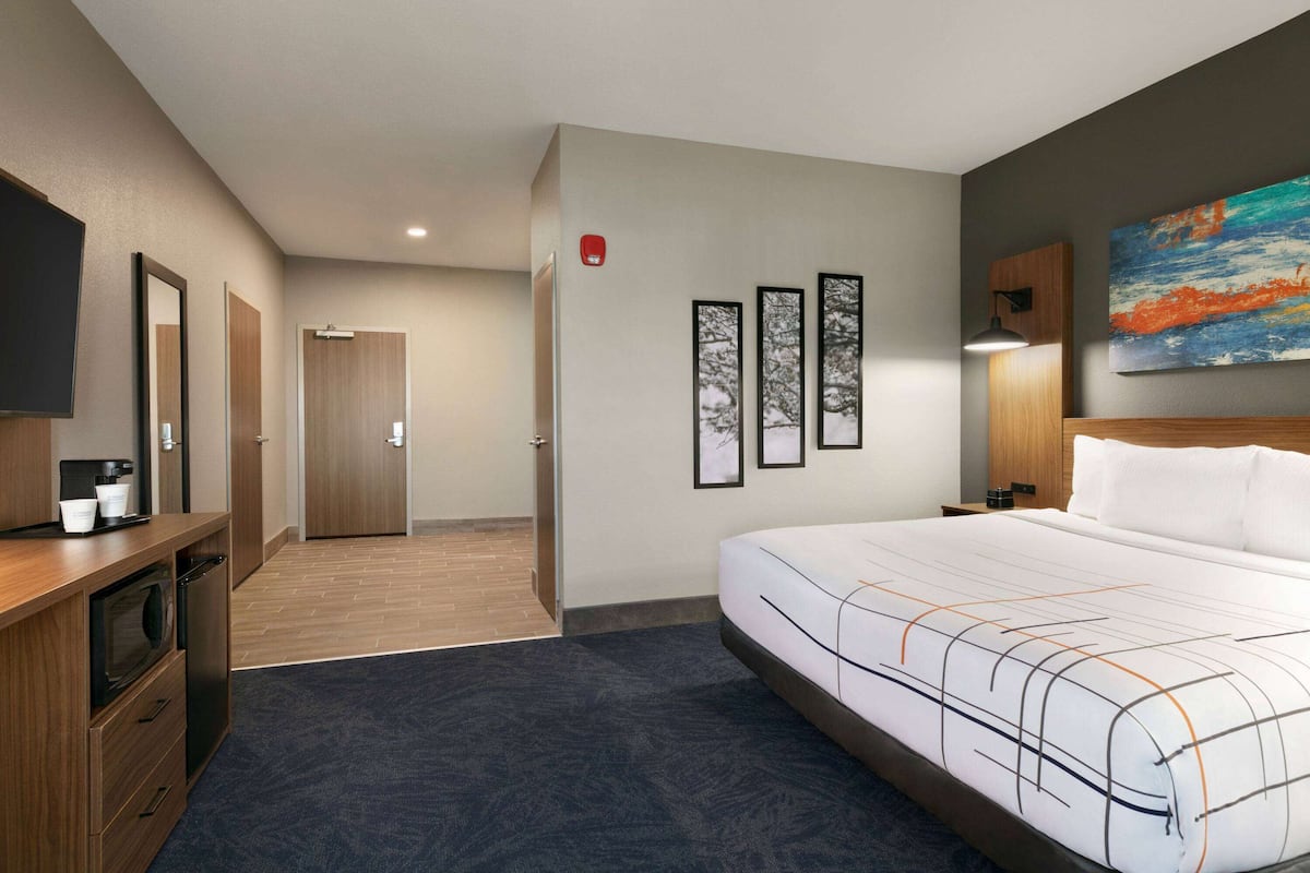 Una habitación de hotel con una cama grande, un escritorio con microondas, cafetera y cuadros en la pared.