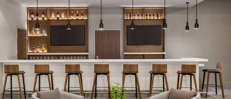 A modern bar area with a long counter, multiple bar stools, and pendant lighting.