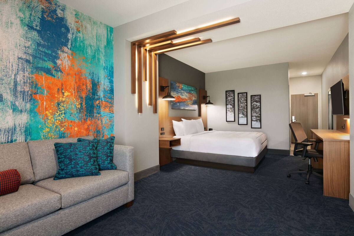 Habitación de hotel con cama, escritorio, sofá y un cuadro abstracto grande en la pared.