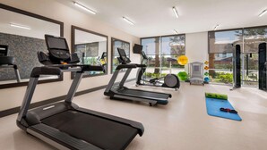 Un gimnasio moderno con cintas de correr, colchonetas de ejercicio y una pantalla de información de estado físico.