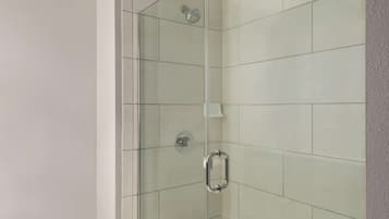 A glass-enclosed shower with a handheld showerhead and a wall-mounted faucet.