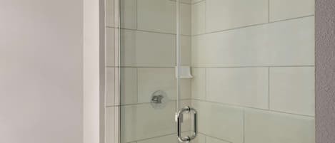 A glass-enclosed shower with a handheld showerhead and a wall-mounted faucet.