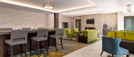 A modern hotel lobby with a bar area, seating arrangements, and a kitchen in the background.