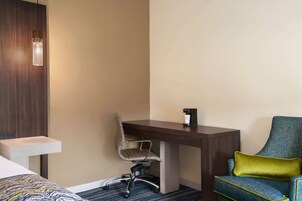Una camera d'albergo con una scrivania, una sedia, un letto e un tavolino con una macchina per il caffè.