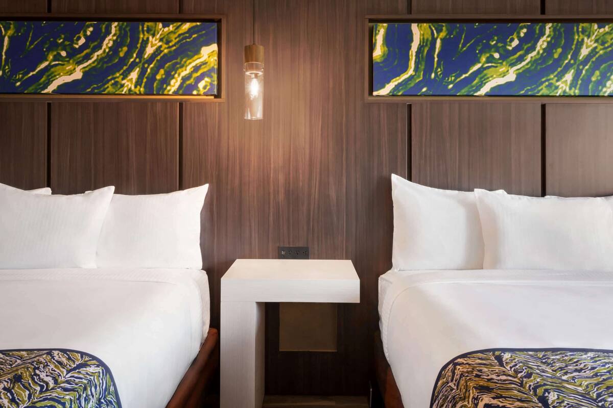 Habitación de hotel con dos camas, una mesita de noche y una lámpara fijada a la pared.