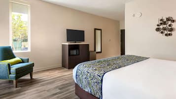A hotel room with a bed, a television on a stand, a chair, and a window with a view of trees.