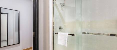 Un baño moderno con cabina de ducha de vidrio, perchero visible y suelo de baldosas.