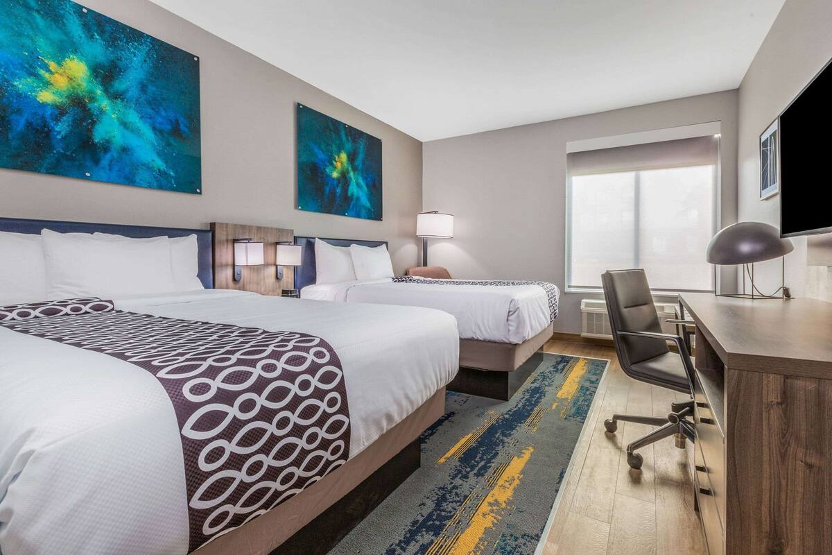 Une chambre d’hôtel avec deux lits, un bureau, une chaise et des œuvres d’art accrochées aux murs.