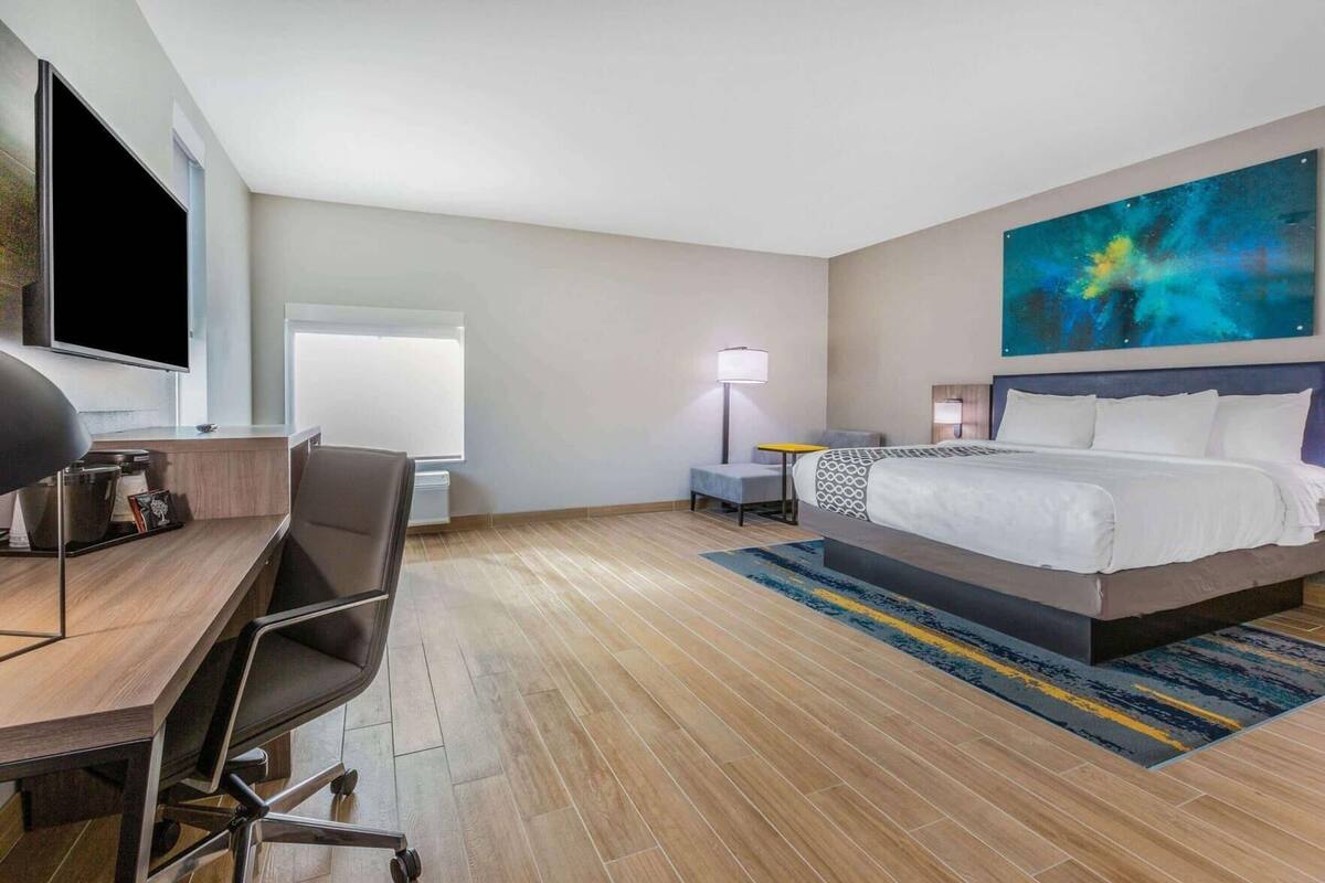 Une chambre d’hôtel avec un lit, un bureau, une chaise, une lampe et un tableau au mur.
