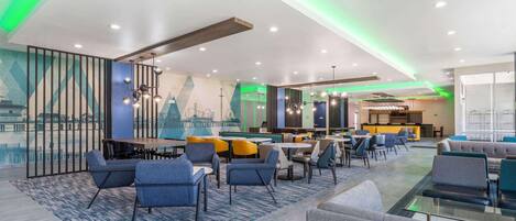 A modern hotel lobby with a dining area, seating arrangements, and a mural on the wall.
