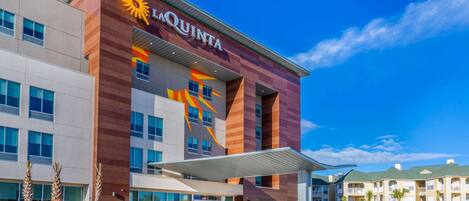 A La Quinta hotel with a modern design, featuring a prominent sun logo and a covered entrance.
