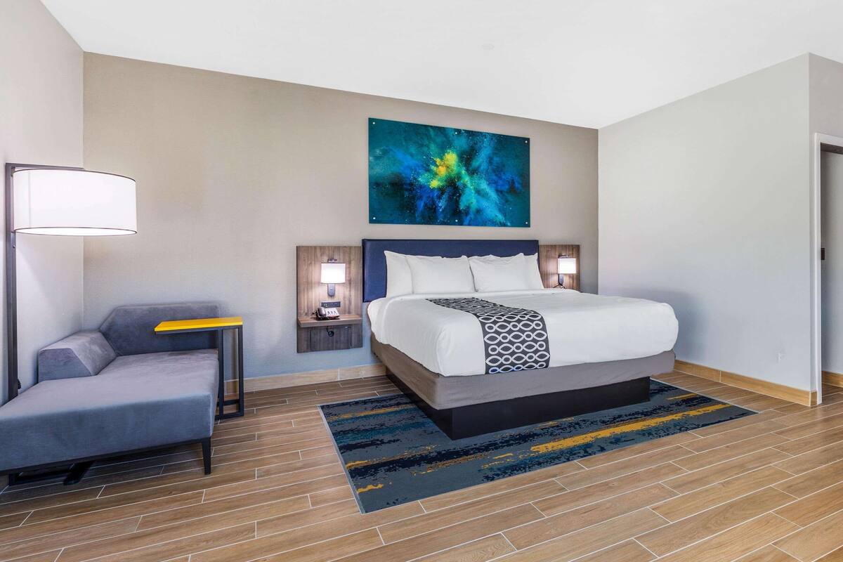 Une chambre d’hôtel moderne, équipée d’un lit, d’un canapé, d’une table de chevet, d’une lampe et d’un grand tableau abstrait accroché au mur.