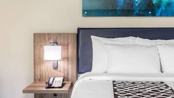 A hotel room with a wooden headboard, a bedside lamp, a telephone, and a bed with white and patterned bedding.