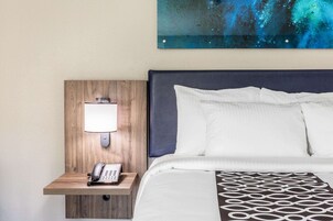 A hotel room with a wooden headboard, a bedside lamp, a telephone, and a bed with white and patterned bedding.