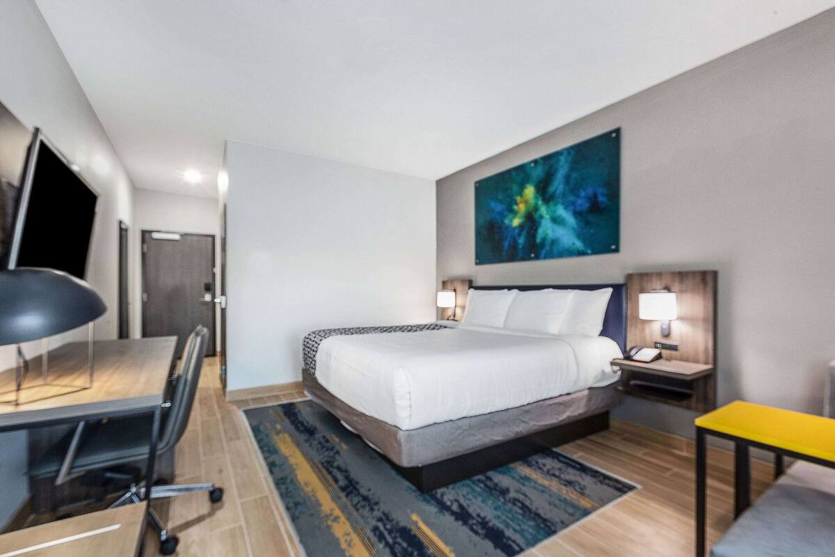 Une chambre d’hôtel avec un lit, un bureau, une chaise, des tables de chevet et un tableau au mur.