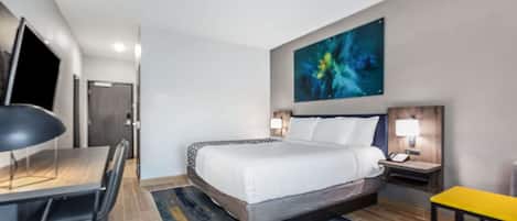 A hotel room with a bed, desk, chair, nightstands, and a painting on the wall.