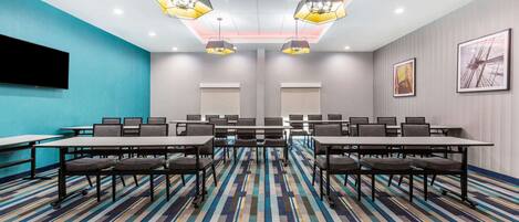 A conference room with a blue accent wall, a large flat-screen TV, and a patterned carpet.