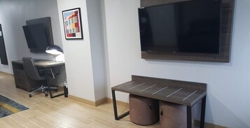 Ein moderner Arbeitsraum mit Schreibtisch, Stuhl und Computer, einem großen Flachbildfernseher und einem gerahmten Bild an der Wand.
