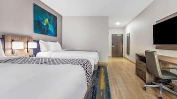 Une chambre d’hôtel avec deux lits, un bureau, une chaise, un téléviseur à écran plat et un tableau au mur.
