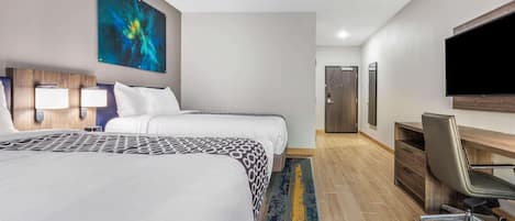 Habitación de hotel con dos camas, un escritorio, una silla, un televisor de pantalla plana y un cuadro en la pared.