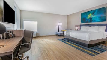 Una habitación de hotel con cama, escritorio, silla, televisor, lámpara y un cuadro en la pared.